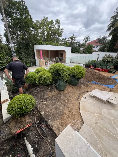 Rear garden under renovation with bagged shrubs, exposed soil and curved paving
