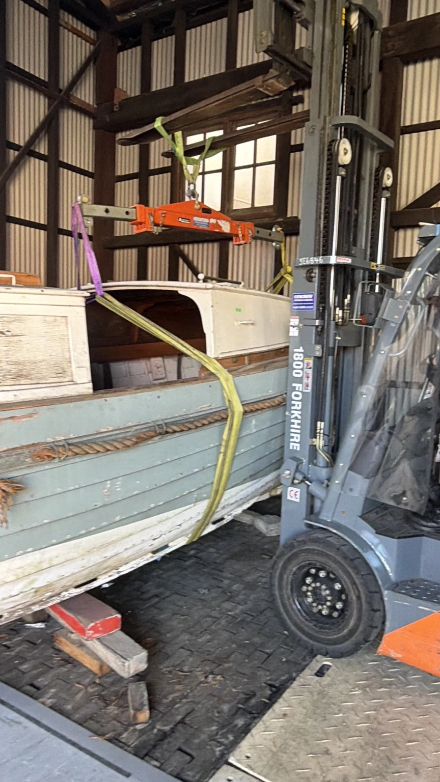 Close view of the forklift beside the boat, with lifting equipment and slings above the hull.