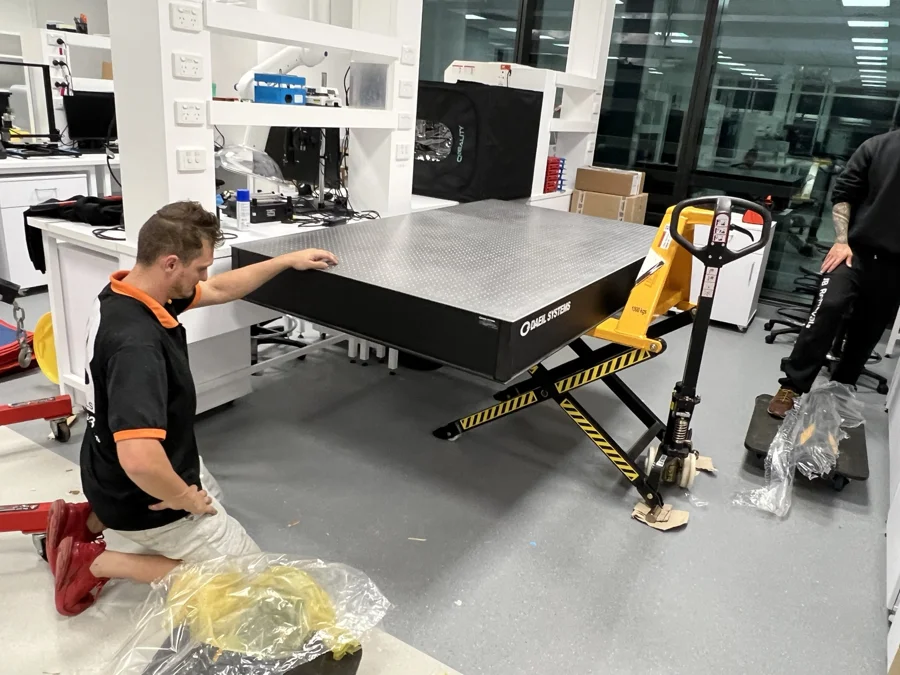 JB crew positioning a precision optical table on a high-lift scissor pallet jack in a laboratory